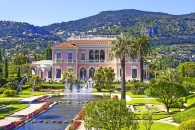 Große Villa inmitten eines gepflegten Gartens mit Springbrunnen und Bergen im Hintergrund.