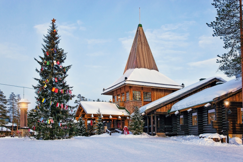Verschneite Landschaft mit dekoriertem Weihnachtsbaum und Holzhäusern.