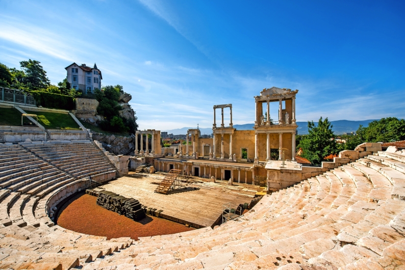 Antikes Amphitheater mit Ruinen und steinernen Sitzreihen unter klarem Himmel.