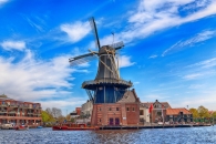 Traditionelle Windmühle an einem Fluss mit blauem Himmel im Hintergrund.