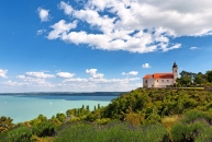 Landschaft mit Kirche auf Hügel und Blick auf einen See unter blauem Himmel.