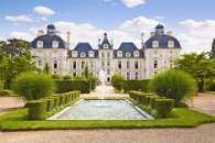 Ein historisches Schloss mit Garten und Brunnen bei sonnigem Wetter.