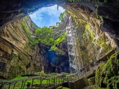 Blick aus einer Höhle nach oben, mit Pflanzen und blauem Himmel sichtbar.