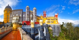 Buntes Schloss auf Hügel mit blauen Himmel und grüner Landschaft.