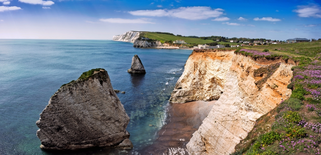 Küstenlandschaft mit weißen Kreidefelsen, blauem Himmel und Meer.