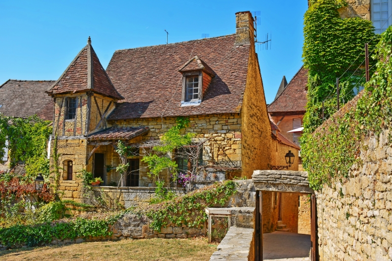 Altes Steinhaus mit Ziegeldach, umgeben von Pflanzen und Efeu, in einer ländlichen Umgebung.