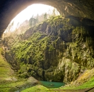 Blick in eine große, moosbedeckte Höhle mit kleinem See am Boden.