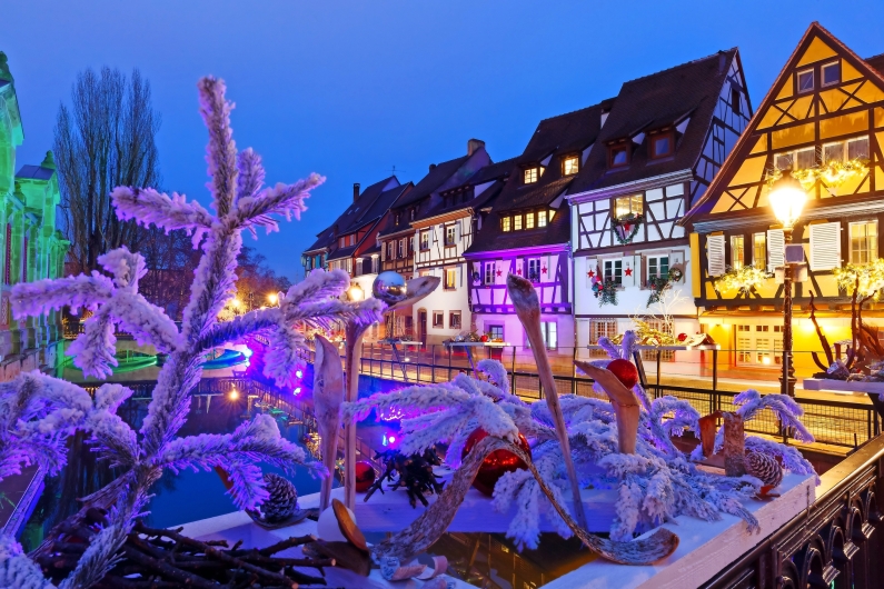 Verschneite Fachwerkhäuser und Dekorationen bei Nacht in Colmar, Frankreich.