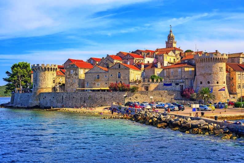 Mittelalterliche Stadt mit Festungsmauern und roten Dächern am Meer.