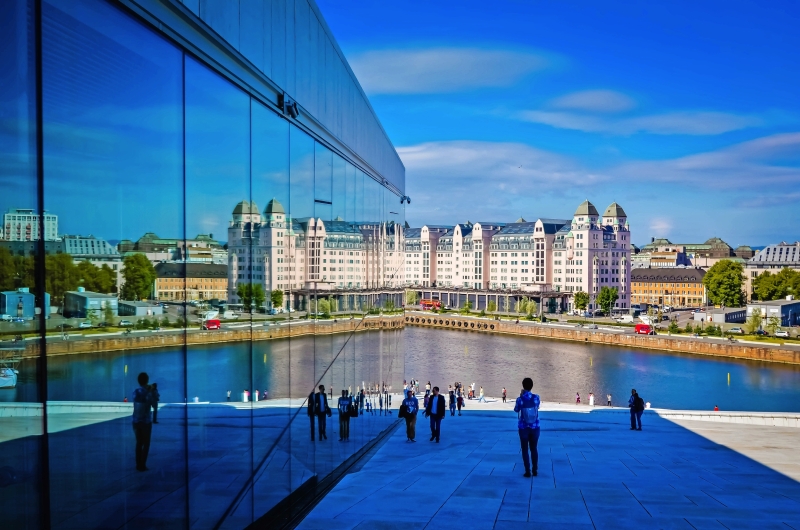 Personen vor moderner Glasfassade mit Blick auf Wasser und historische Gebäude im Hintergrund.