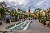 Platz mit Springbrunnen und Palmen, umgeben von historischen Gebäuden.