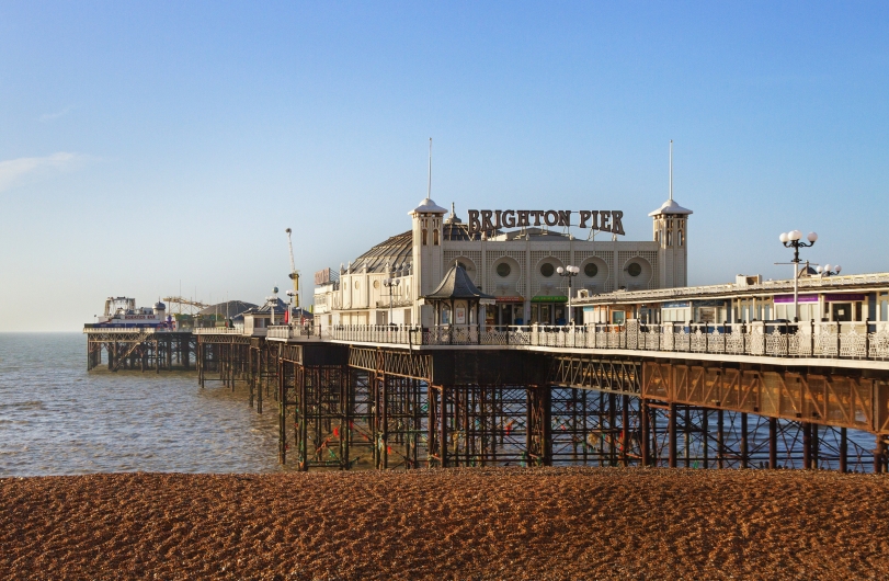 Brighton Pier bei sonnigem Wetter mit Kieselstrand im Vordergrund.